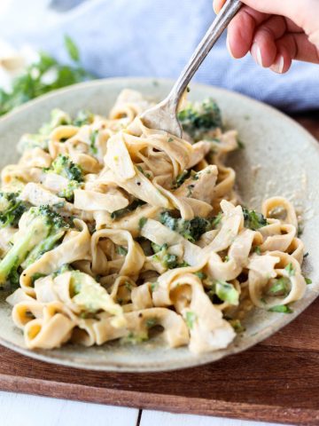 Fork swirling pasta with chicken alfredo with broccoli.