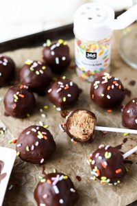 Vanilla cake pops dipped in chocolate with rainbow sprinkles.