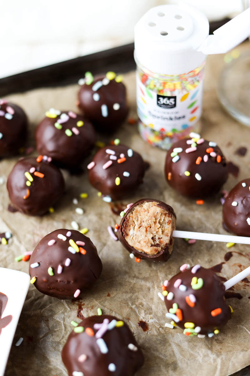 Vanilla cake pops dipped in chocolate with rainbow sprinkles.