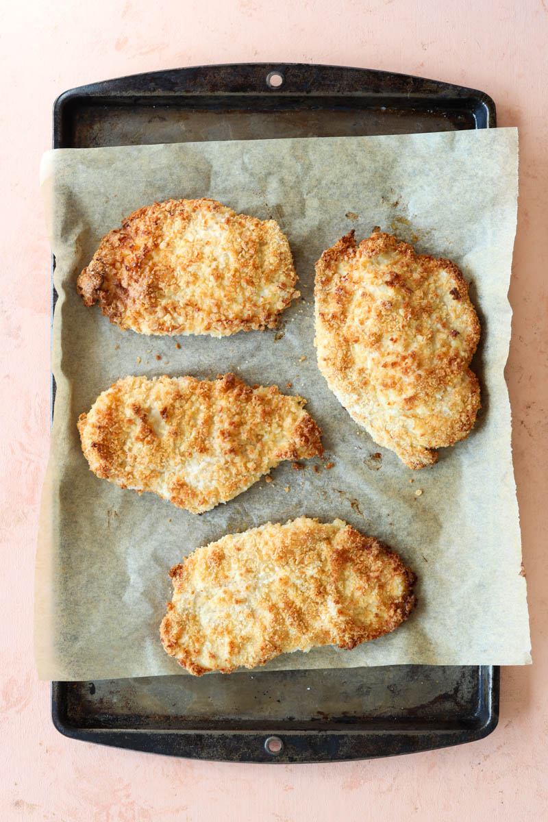 Crispy chicken cutlets on a parchment paper lined baking sheet.