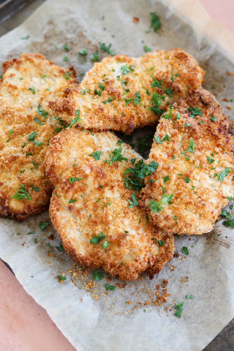 Chicken cutlets laying on a baking sheet.