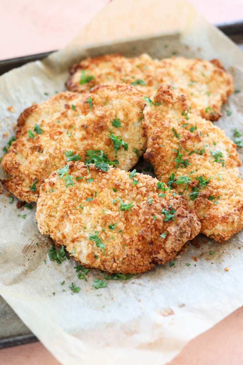 Chicken cutlets on a parchment paper lined baking sheet.