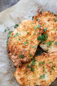 Close up picture of chicken cutlets with parsley on top.