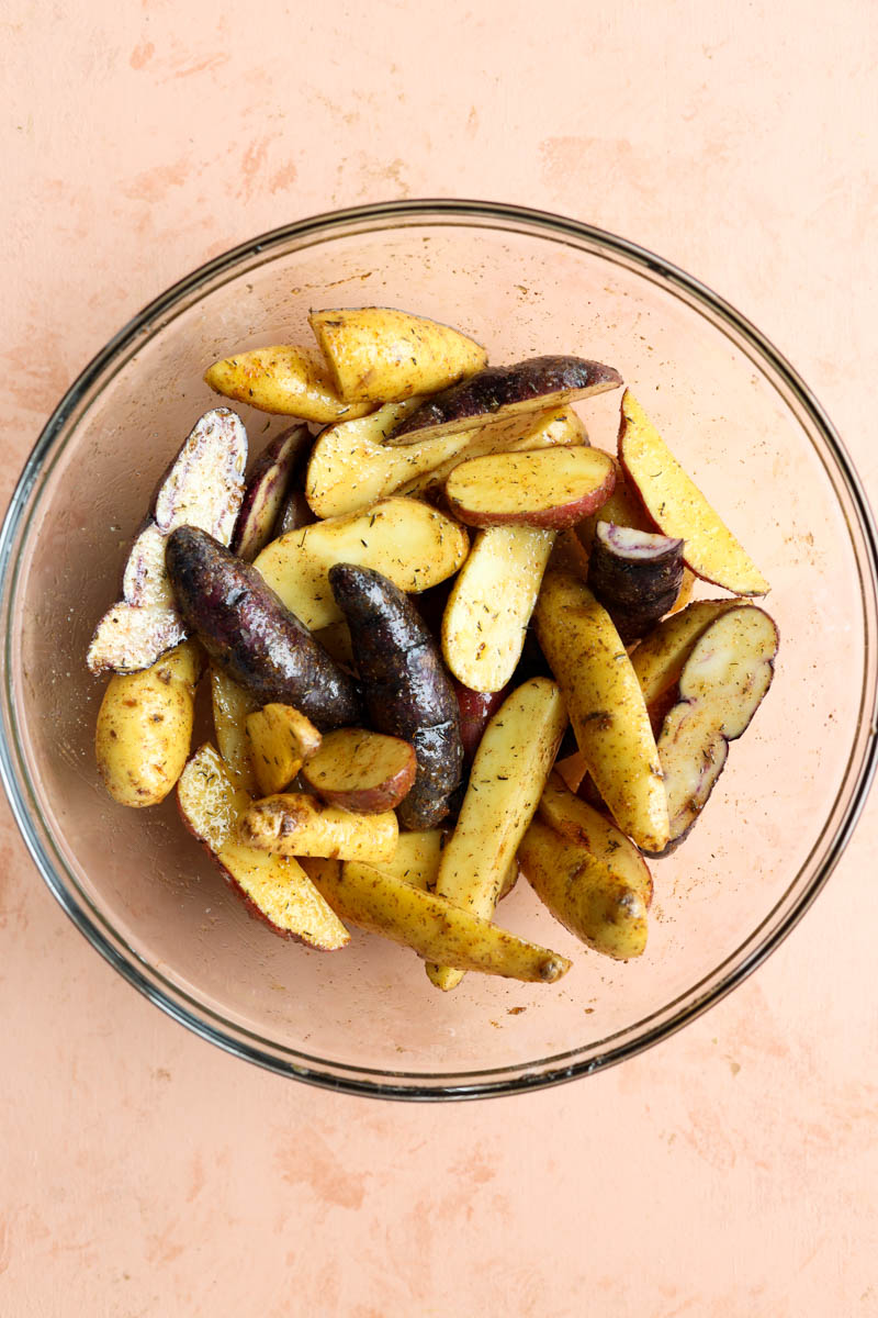 Bowl of fingerling potatoes with oil and seasoning.