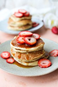 Syrup drizzled over banana pancakes with fresh strawberry slices.
