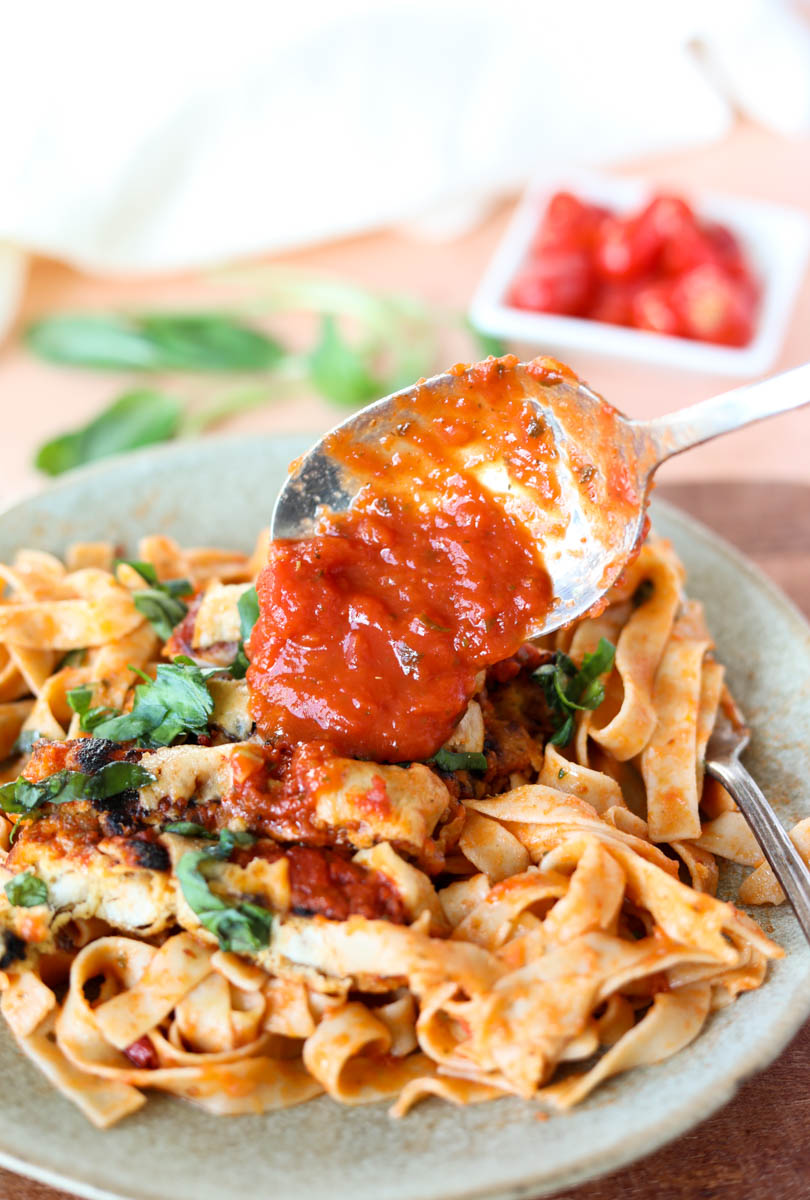Pouring sauce over pasta and chicken parm.