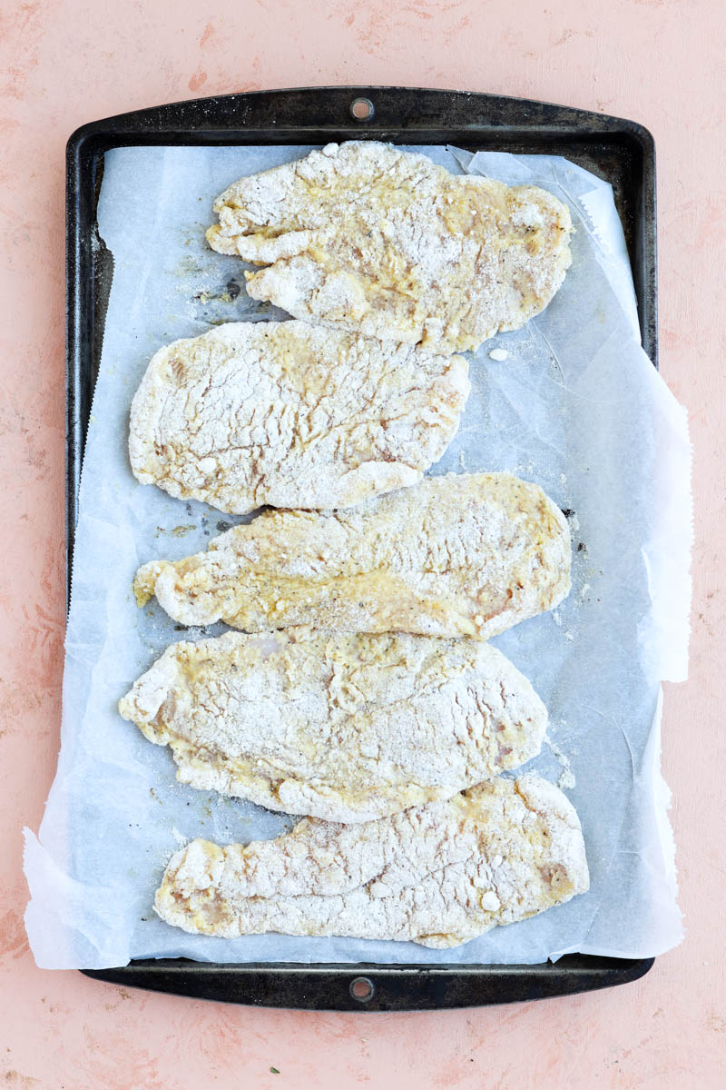 Breaded chicken cutlets on a parhcment paper lined baking sheet.