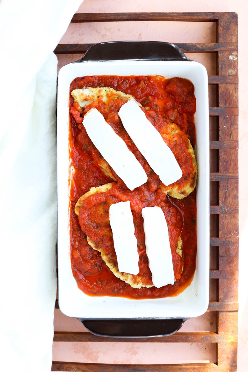 Chicken with sauce and dairy free cheese in baking sheet.