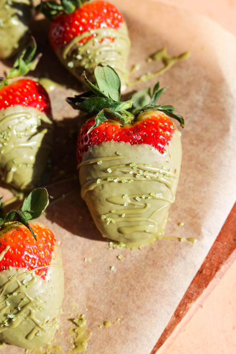 Close up of large chocolate covered strawberry with green sprinkles.