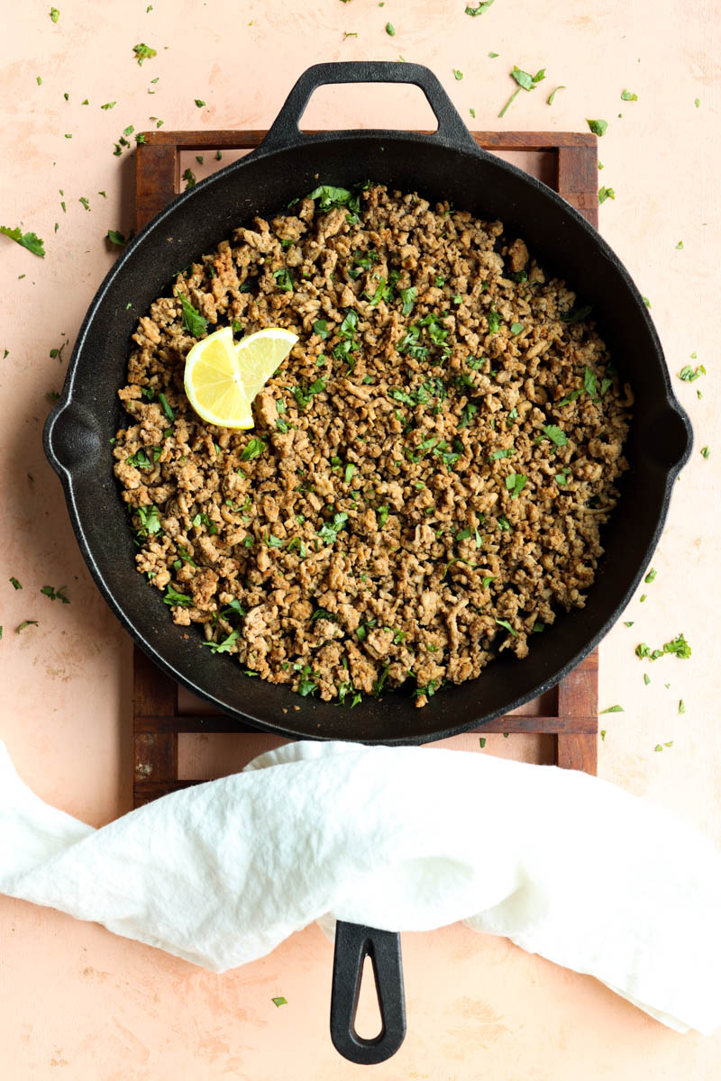 Ground turkey in a cast iron skillet with lemon wedges.