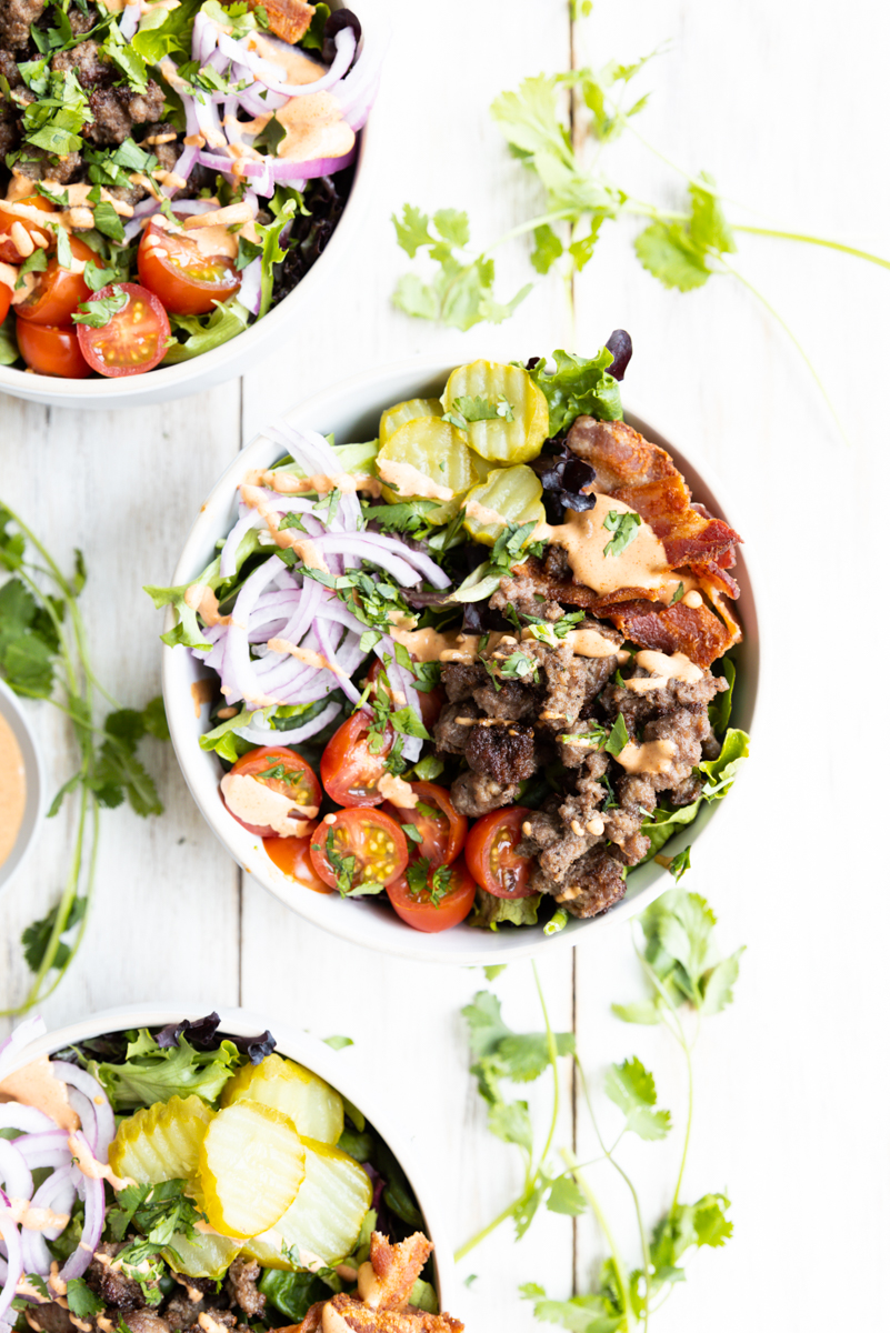 Burger bowls lined up on a wooden board with fresh cilantro.