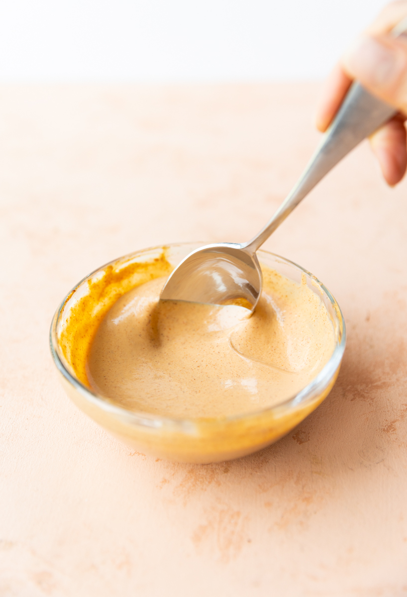 Spoon stirring spicy burger sauce in a glass bowl.