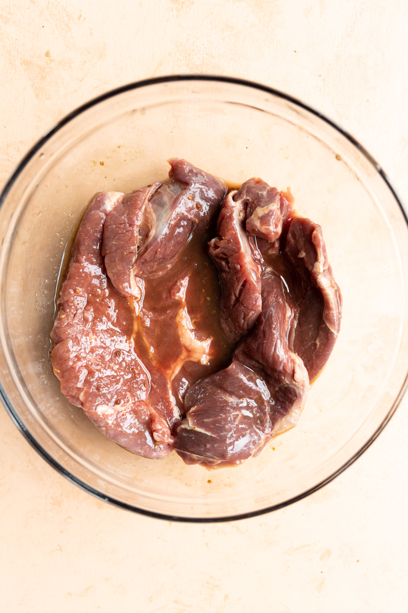 Beef marinating in glass bowl.