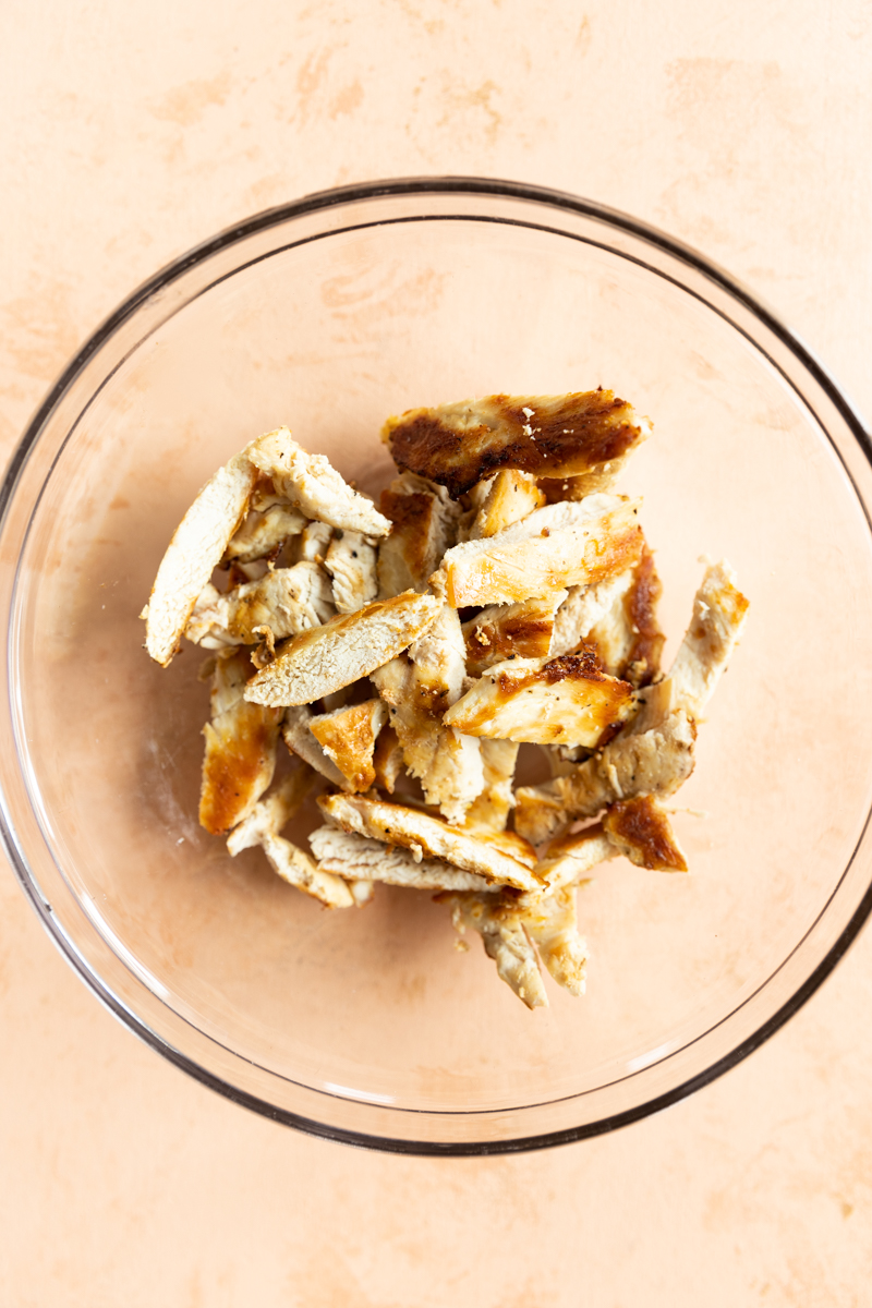 Sliced chicken in a glass mixing bowl.