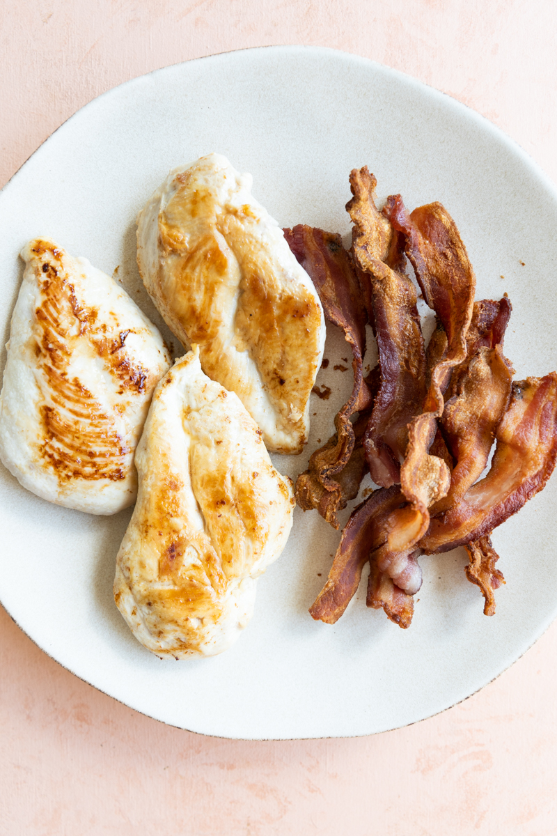 Cooked chicken breast and bacon on a white plate.