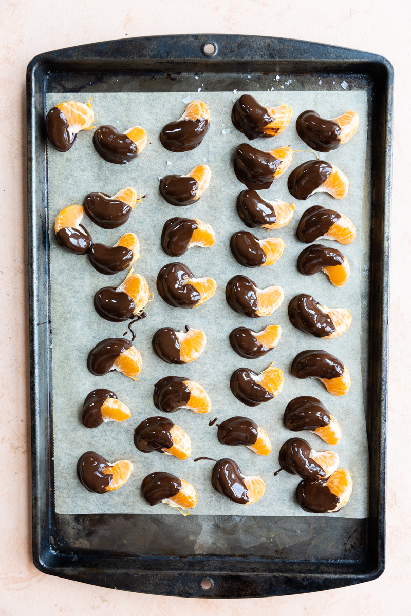 Oranges slices dipped in chocolate cooling on a baking sheet.