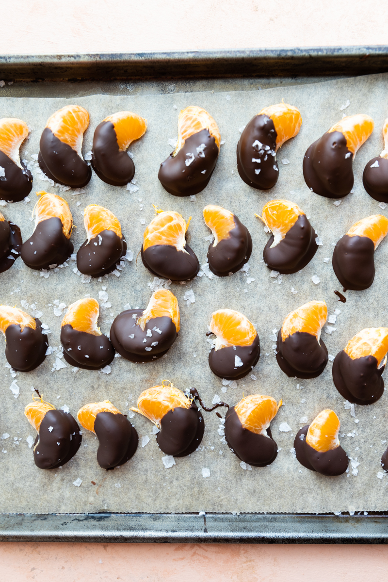 Chilled orange slices on a parchment paper lined baking sheet with flaky sea salt.