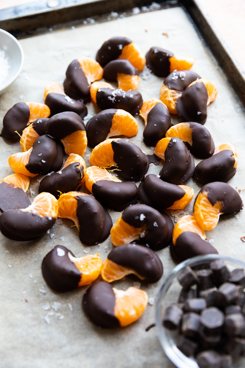Chocolate covered oranges on a parchment paper lined baking sheet.