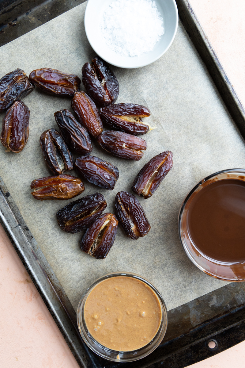 Melted chocolate, crunchy peanut butter, and pitted dates on a baking sheet.