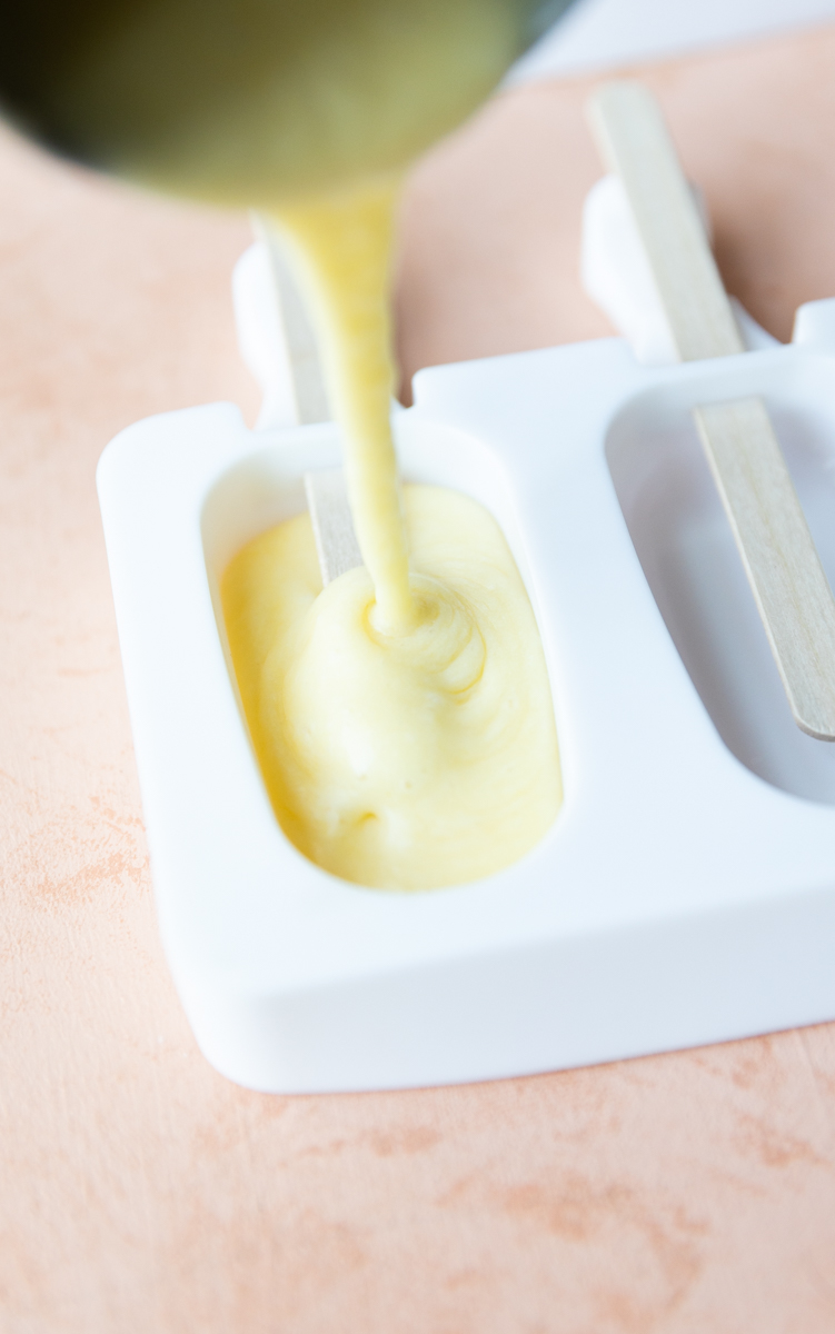 Pouring orange ice cream bars in popsicle mold.