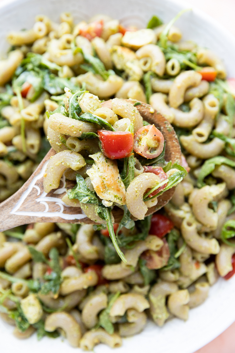 Wooden spoon holding up big scoop of pesto chicken pasta salad.