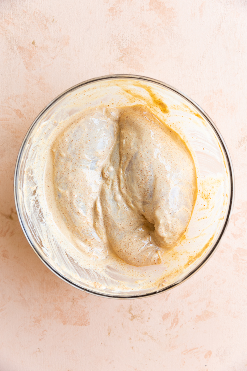 Chicken marinating in glass bowl.