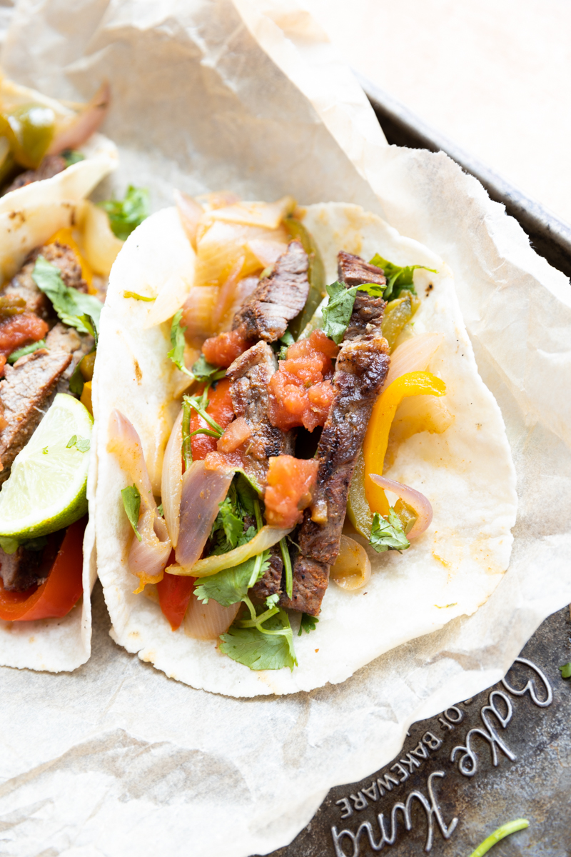 Steak fajita tacos on a parchment paper lined baking sheet.