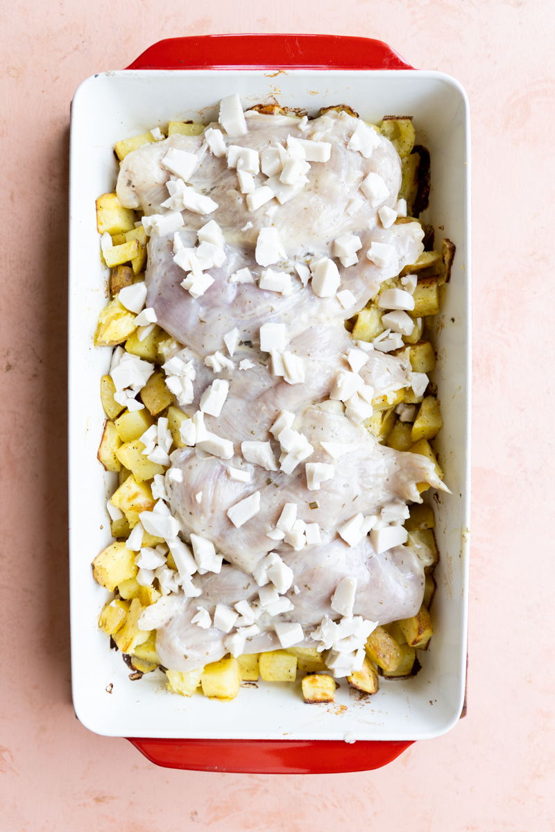 Baked potatoes with marinated chicken and cheese on top before going in the oven.