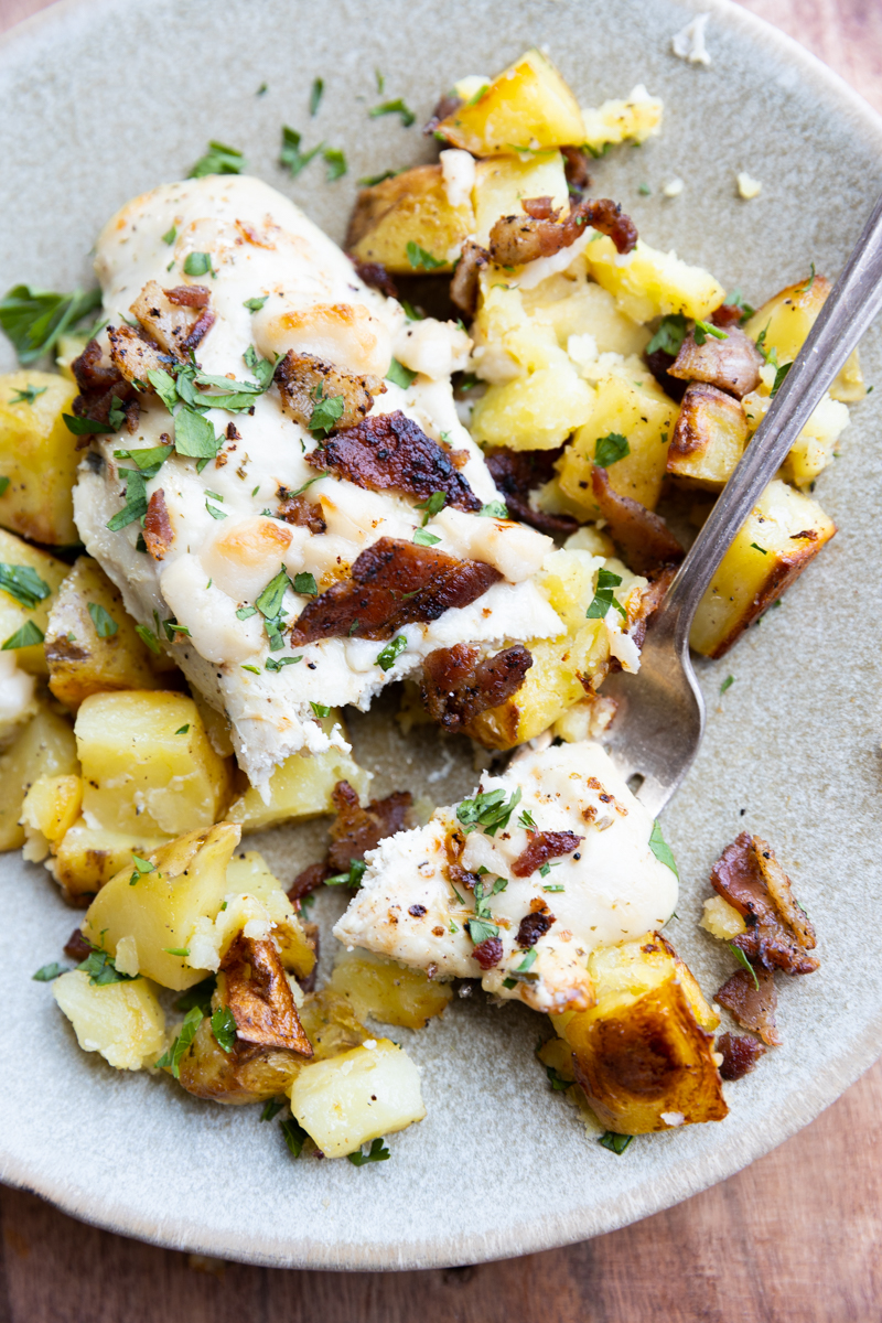 White plate with chicken and potatoes with bacon pieces.