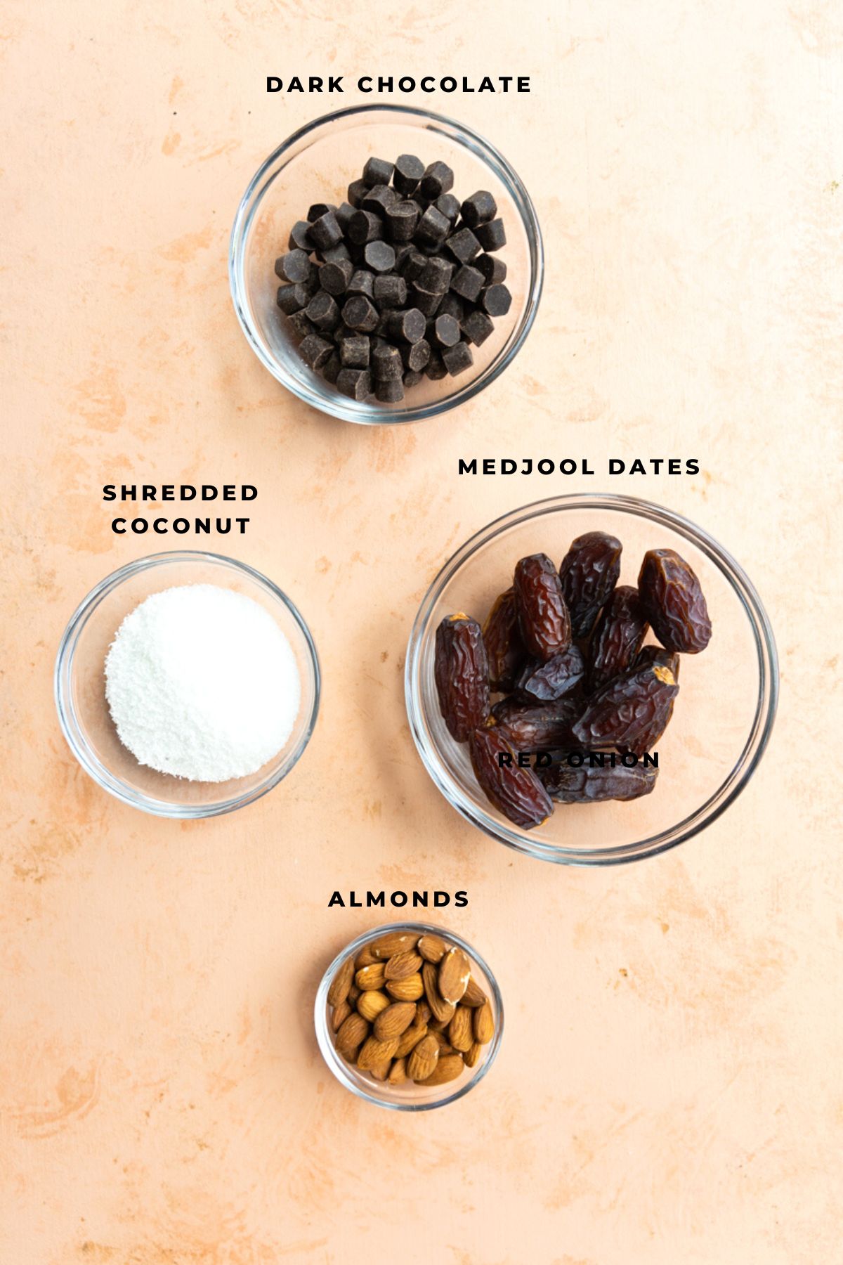 Chocolate chips, medjool dates, shredded coconut, and almonds in small bowls.