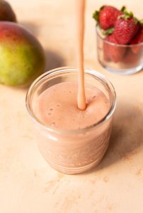 Strawberry mango banana smoothie being poured into a glass.