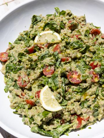 Pesto orzo salad in a white bowl with lemon slices on top.