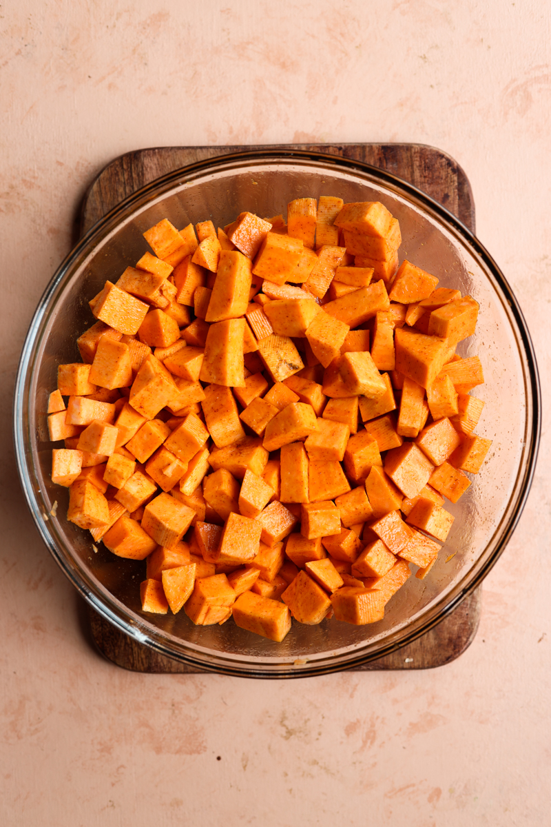 Bowl of cubed sweet potato tossed in olive oil, paprika, garlic powder, and salt.
