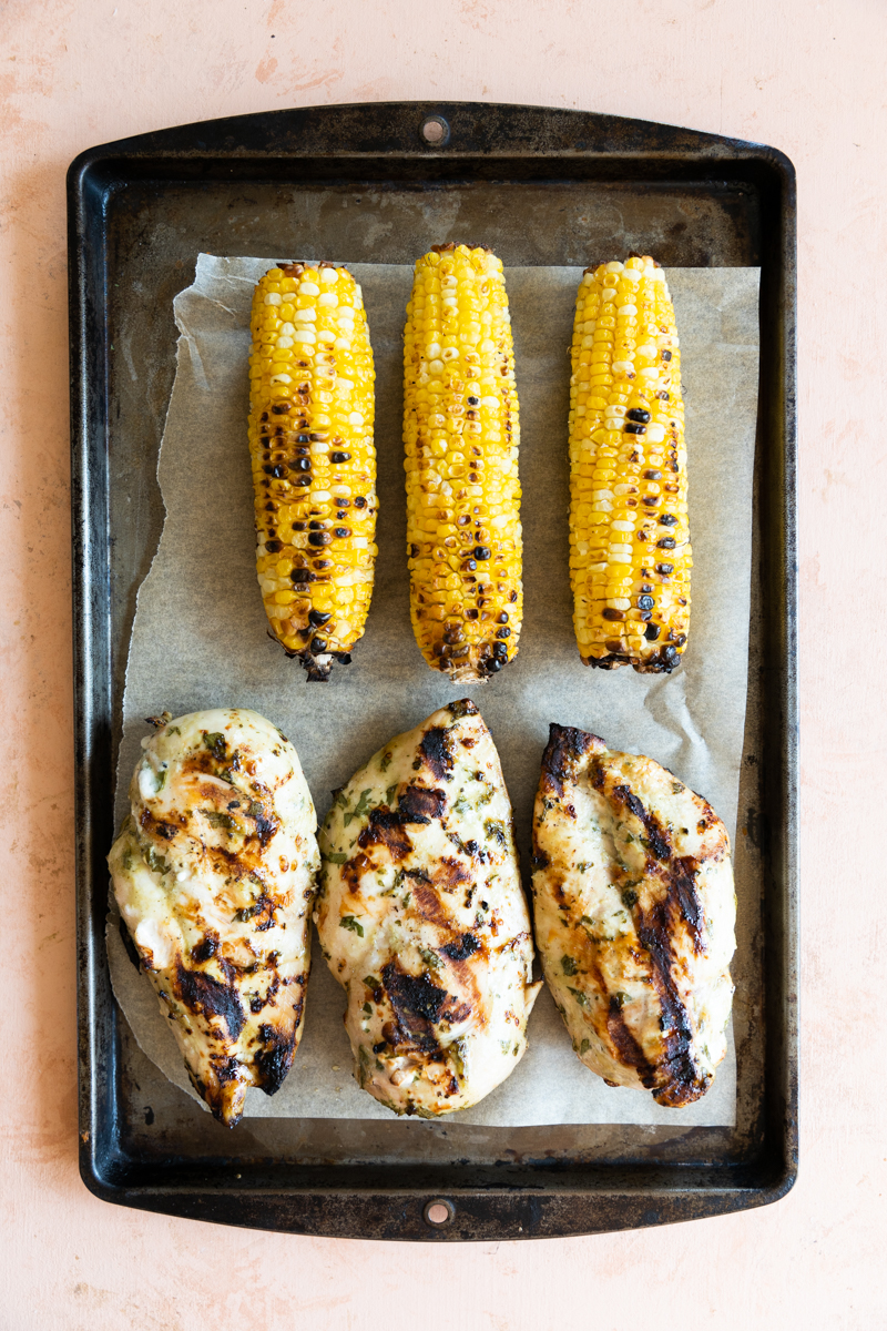 Grilled corn and grilled chicken on a baking sheet.