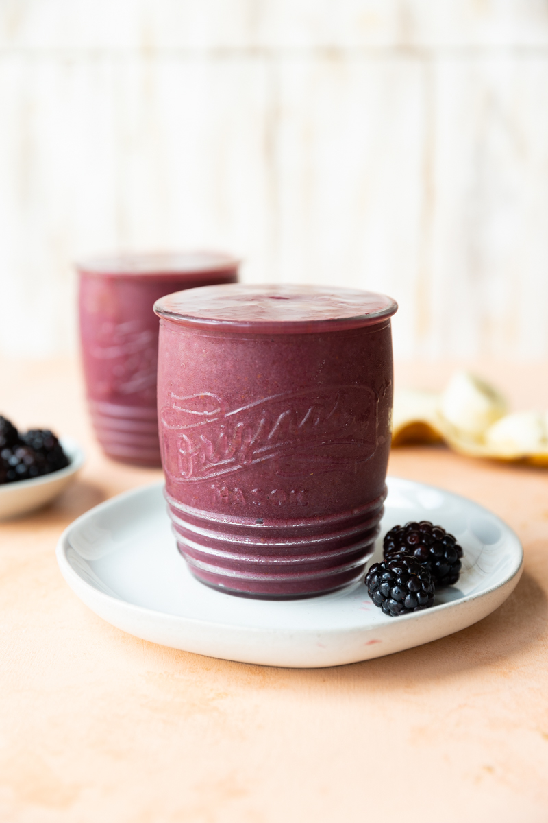 Blackberry smoothie on a plate with two blackberries on the side.