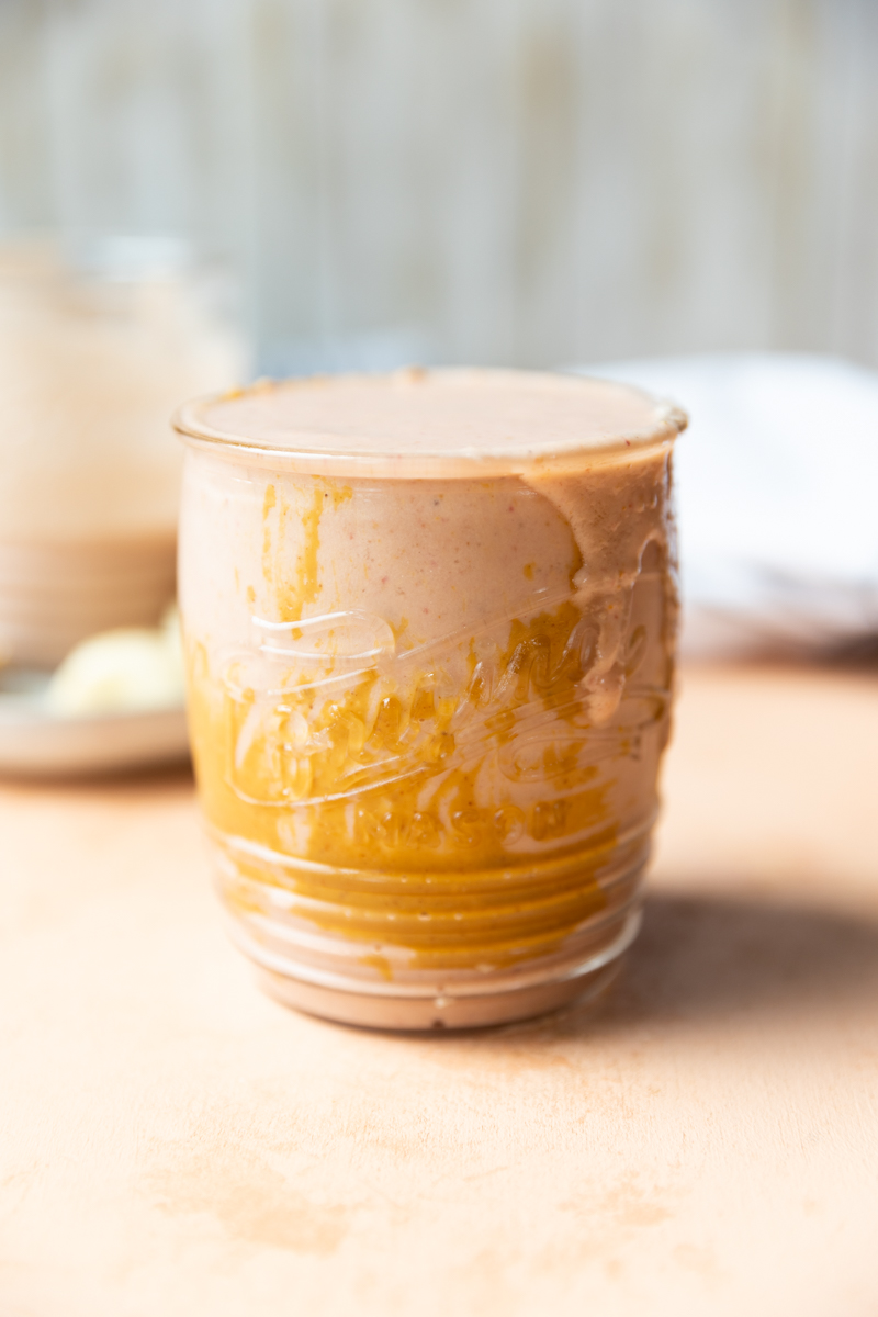 Peanut butter smeared on the inside of glass cup holding strawberry banana smoothie.