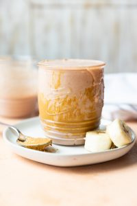 Smoothie on a plate with spoon dipped in peanut butter.