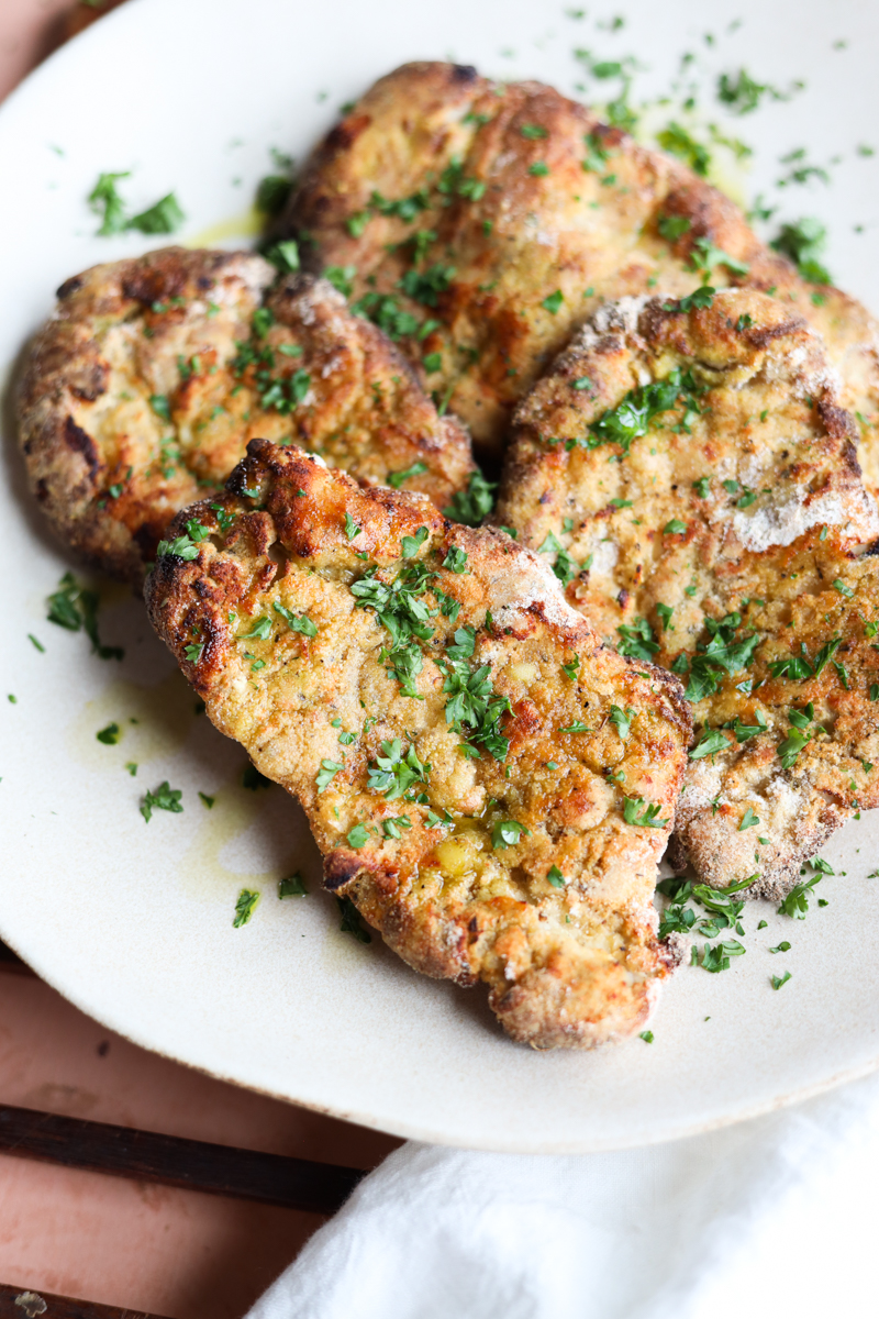 Crispy chicken cutlets on plate with chopped parsley on top.