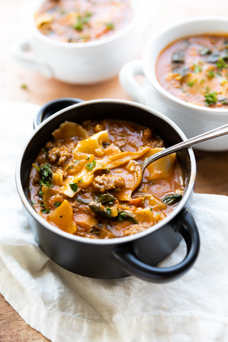 Lasagna soup in a black bowl with spoon sticking out.