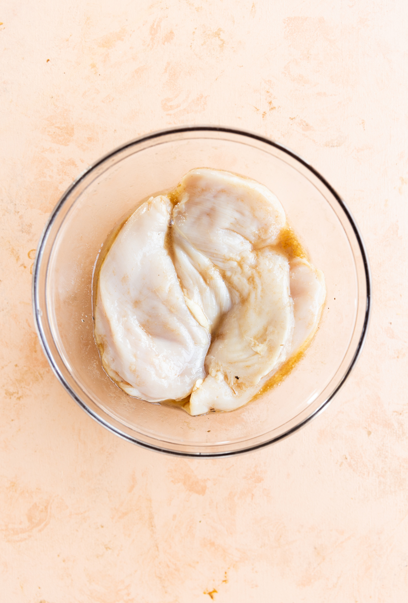 Chicken breast marinating in glass mixing bowl.