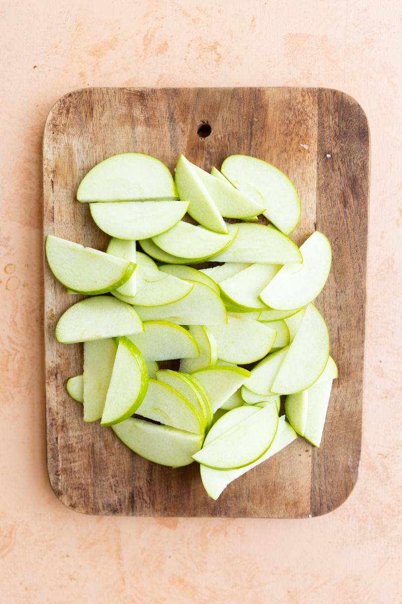 Green apples sliced on a wooden cutting board.