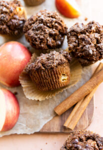 Apple crumble muffins on parchment paper with cinnamon sticks and apples.