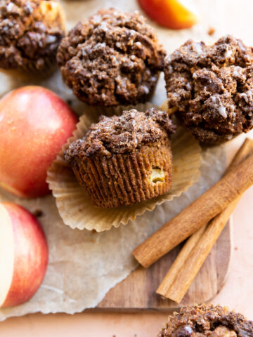 Apple crumble muffins on parchment paper with cinnamon sticks and apples.
