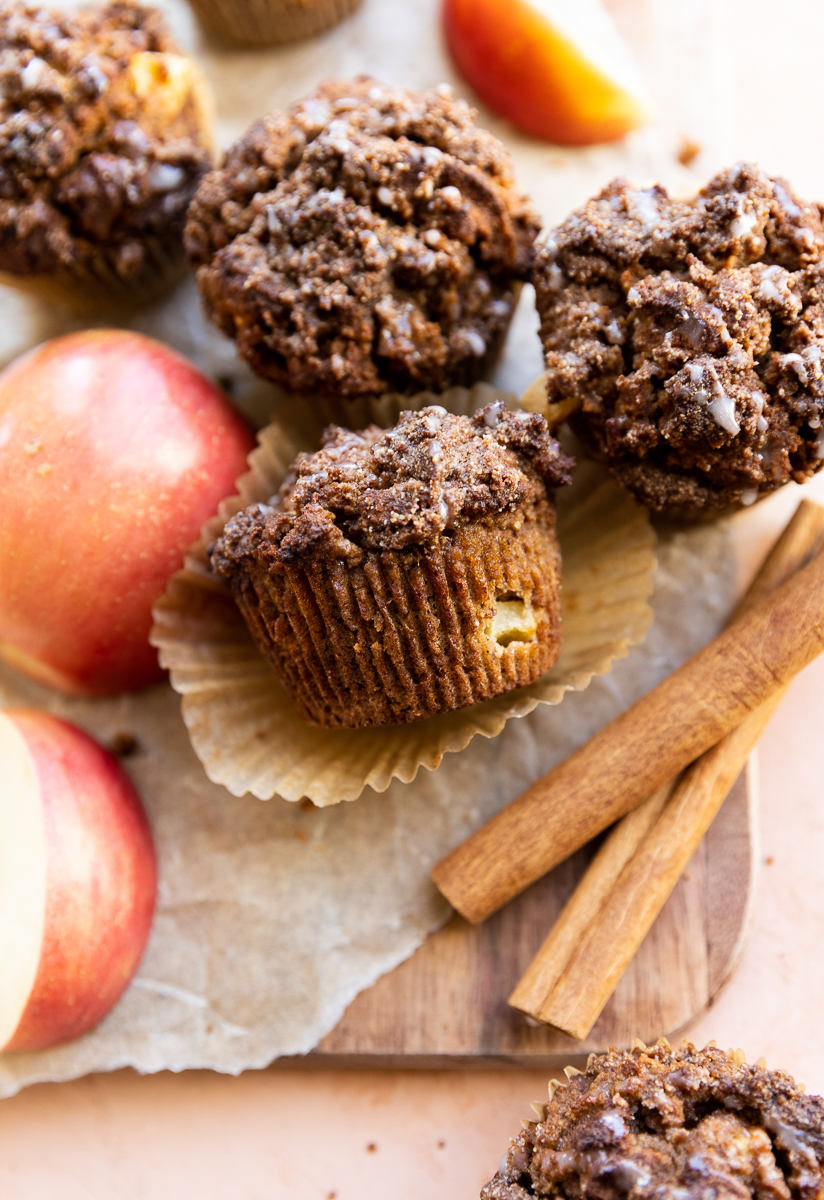 Apple crumble muffins on parchment paper with cinnamon sticks and apples.