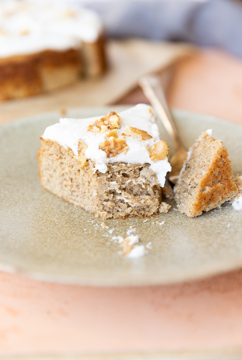 Slice of banana cake with coconut cream frosting on a ceramic plate.