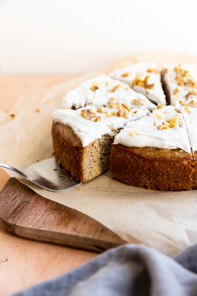 Gluten free banana cake with frosting and crumbled walnuts on top.