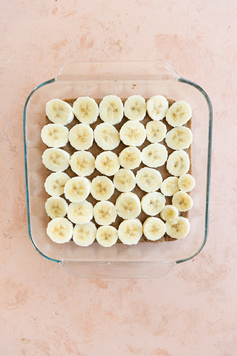 Baked crust layered with bananas in baking pan.