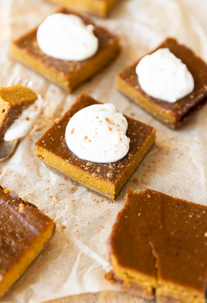Pumpkin pie bars on parchment apper with coconut whipped cream dollop on top of each bar.