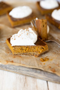 Pumpkin pie bar with a bite taken out on a fork in the background.