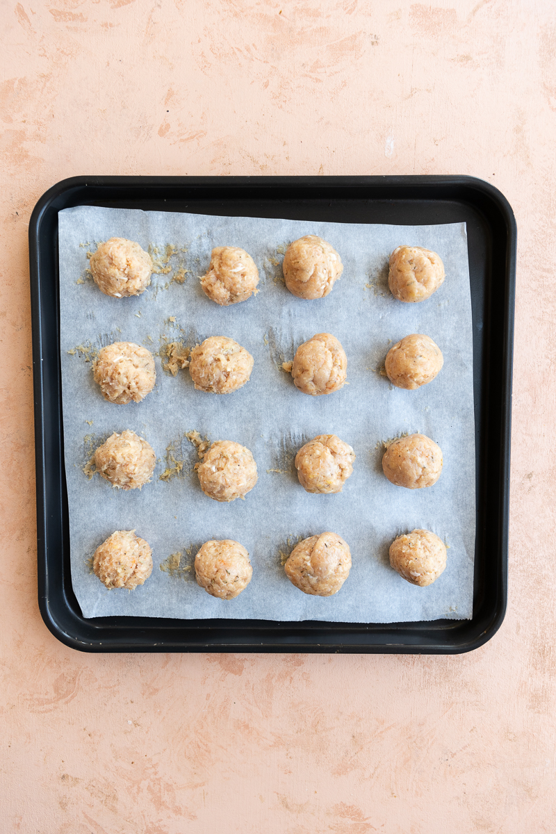 Uncooked chicken meatballs on parchment paper lined sheet.